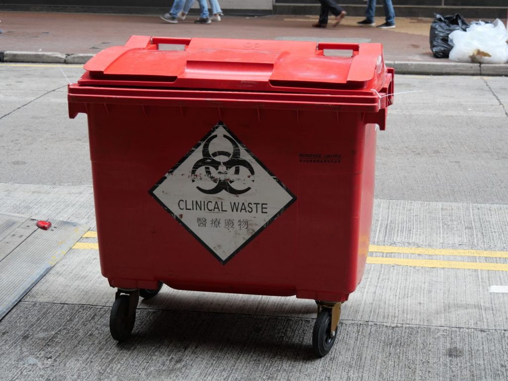 A red wheeled bin labeled for clinical waste management on a city street.