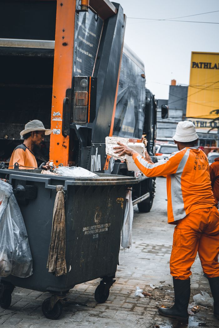 Home Sanitation workers disposing garbage into a truck on city street.