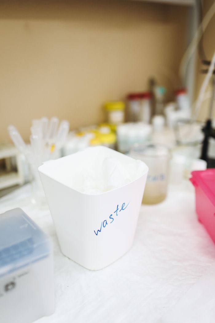About White waste bin in a laboratory setting, surrounded by glassware and containers.