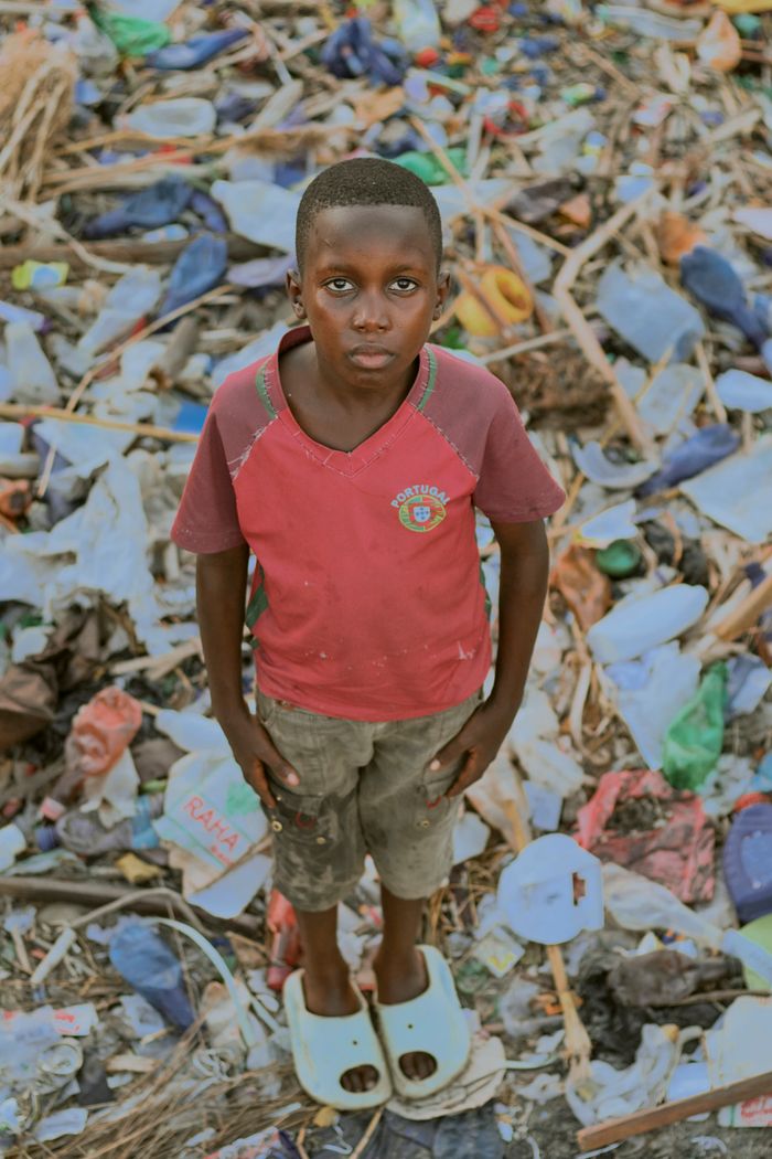 A young boy stands in a pile of urban waste, reflecting environmental concerns.
